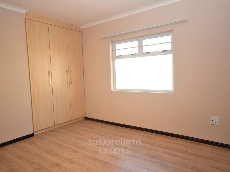 A clean, empty bedroom featuring light wood-look laminate flooring and a built-in wardrobe with matching wood-tone finish.