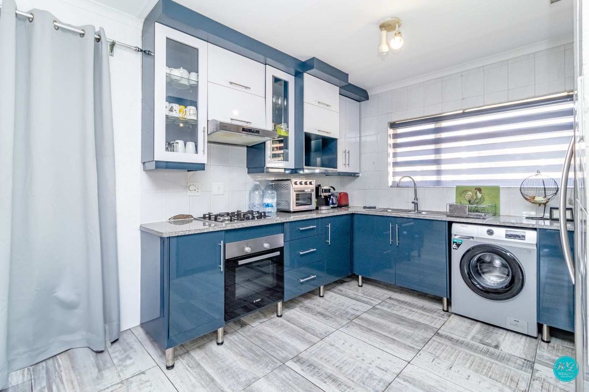 Modern kitchen featuring blue and white cabinetry, granite countertops, gas hob, built-in oven, and integrated laundry plumbing with tiled flooring.