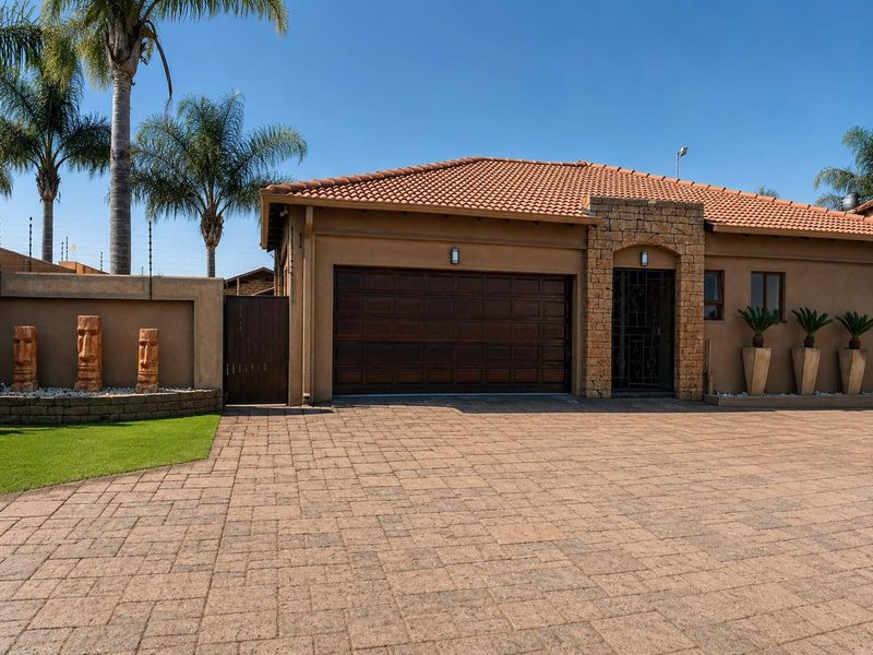 Front elevation of a townhouse featuring a paved driveway, double garage, stone-clad entrance, and well-maintained boundary wall with electric fencing.