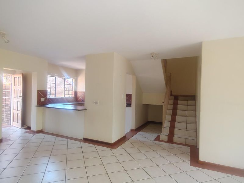 Open plan living area featuring tiled flooring, a staircase, and a functional kitchen layout with a breakfast counter.