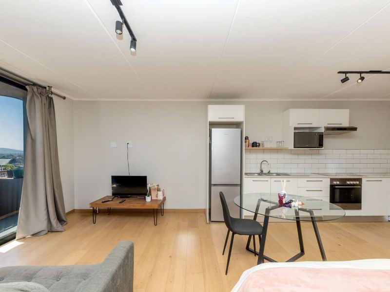 Modern open-plan living area featuring a well-equipped kitchen with subway tile backsplash, integrated appliances, and direct access to a balcony with scenic views.