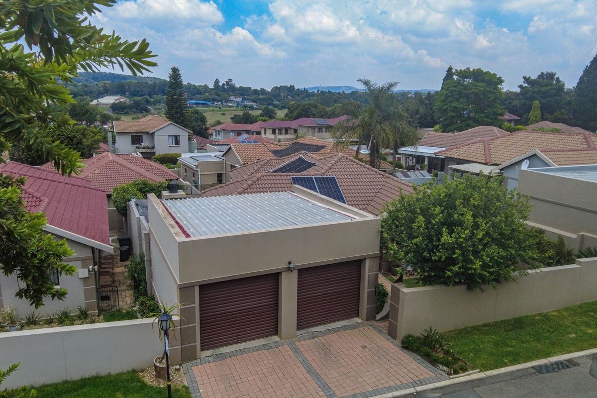 Aerial view of a residential property featuring a double garage with roller doors, paved driveway, and tiled roof with solar panels in a suburban estate.