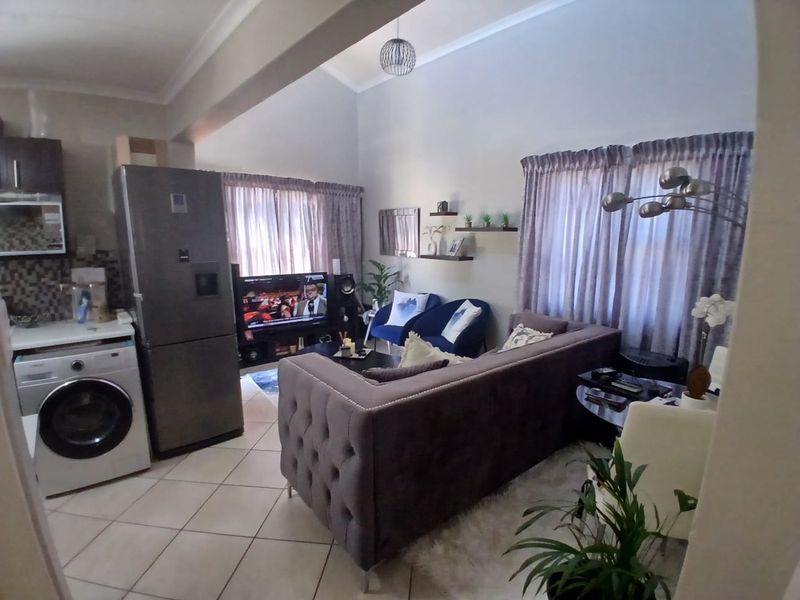 An open-plan living area featuring tiled flooring, a vaulted ceiling, and a compact kitchen section with built-in cabinetry and a mosaic backsplash.