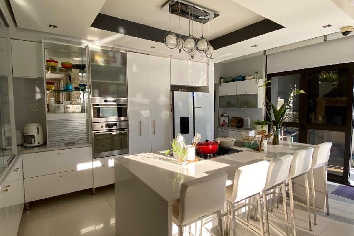Modern kitchen featuring a central island with breakfast bar seating, built-in oven, microwave, and sleek cabinetry under a recessed ceiling with integrated lighting.