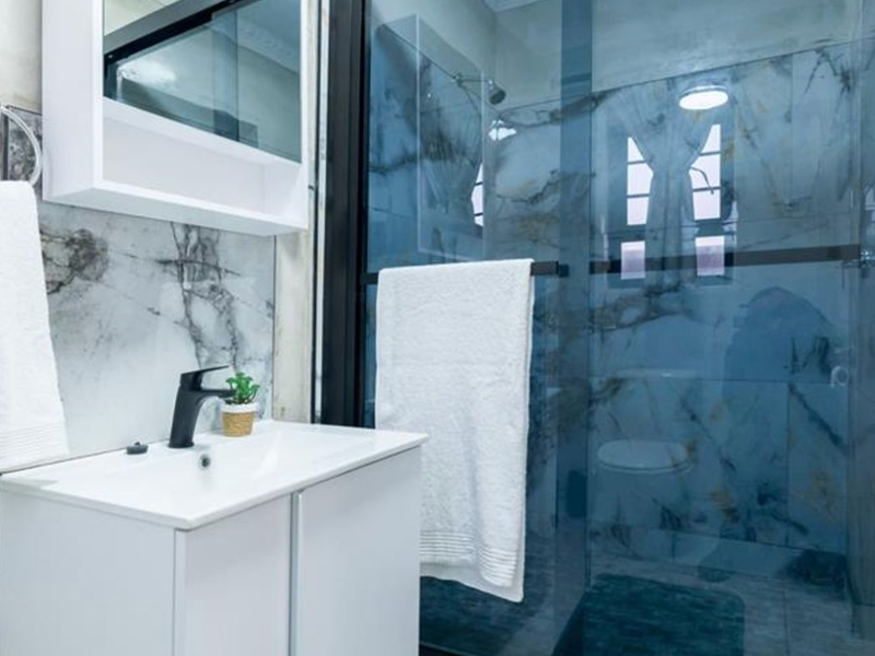Modern bathroom featuring a sleek vanity with black mixer tap, marble-look wall tiling, and a glass-enclosed shower area.