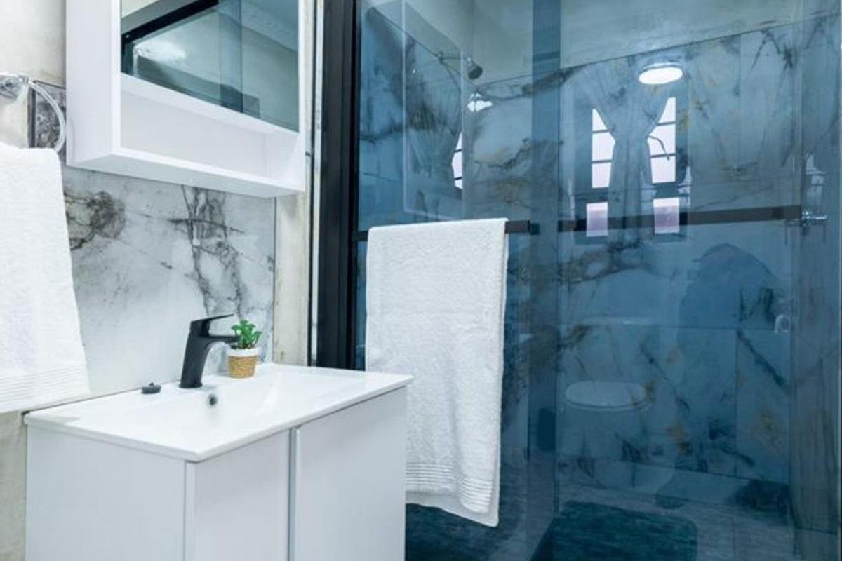 Modern bathroom featuring a sleek vanity with black mixer tap, marble-look wall tiling, and a glass-enclosed shower area.