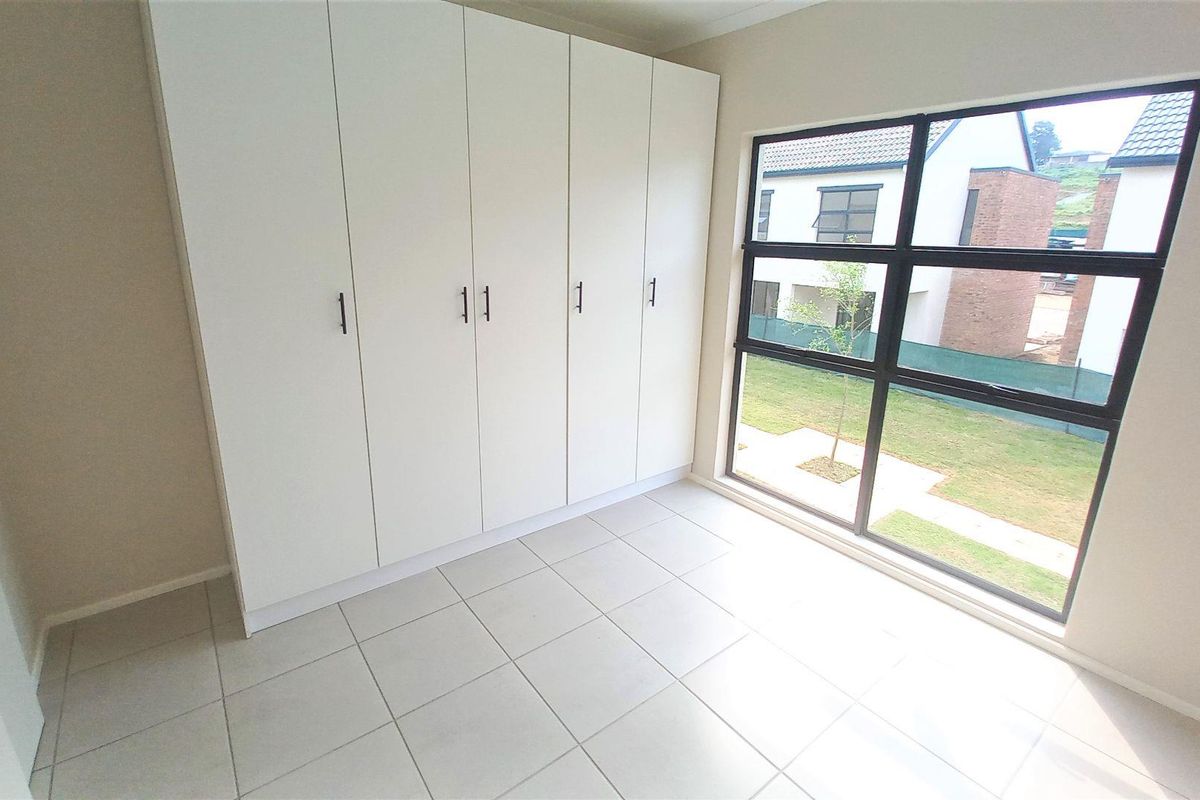 A bright, empty bedroom featuring neutral floor tiles and a large, modern built-in wardrobe with clean white cabinetry.