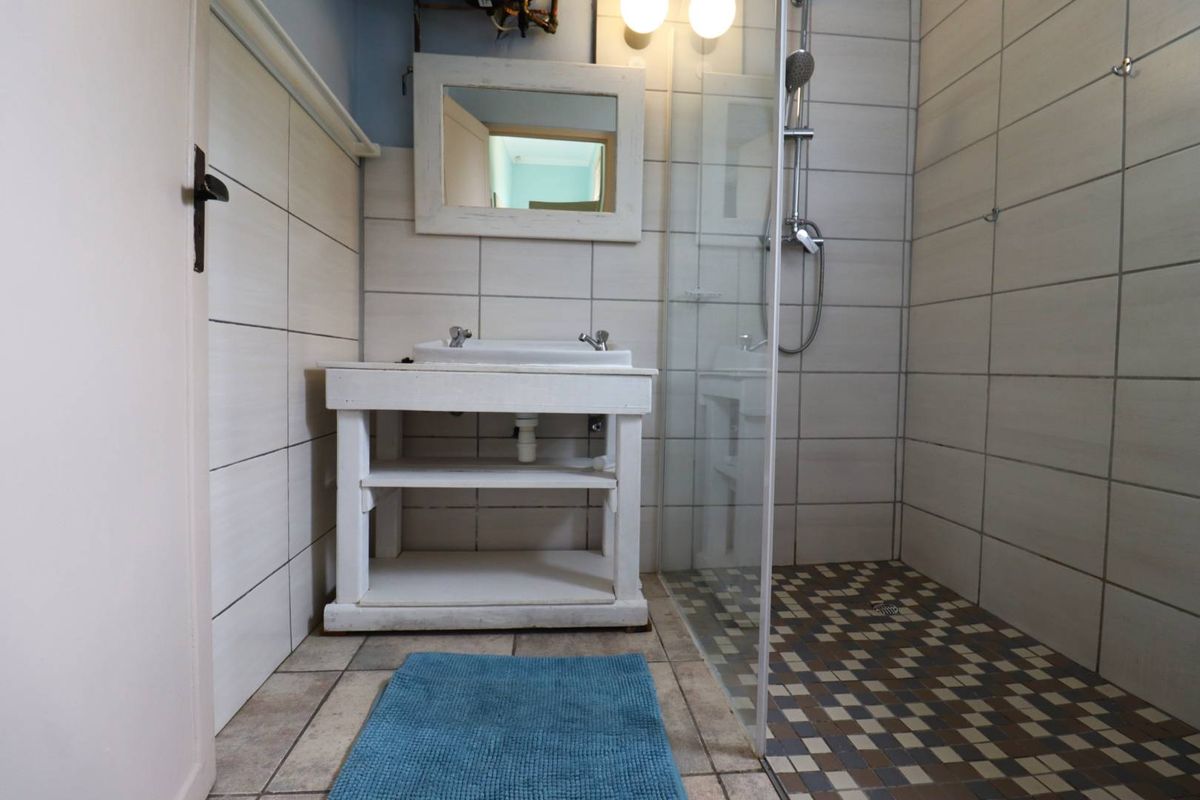 A functional bathroom featuring a walk-in shower with glass enclosure, a vanity basin, and tiled wall and floor finishes.