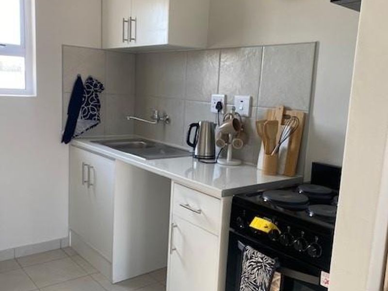Compact kitchen featuring white cabinetry, tiled splashback, stainless steel sink, and a freestanding stove with ceramic floor tiles.