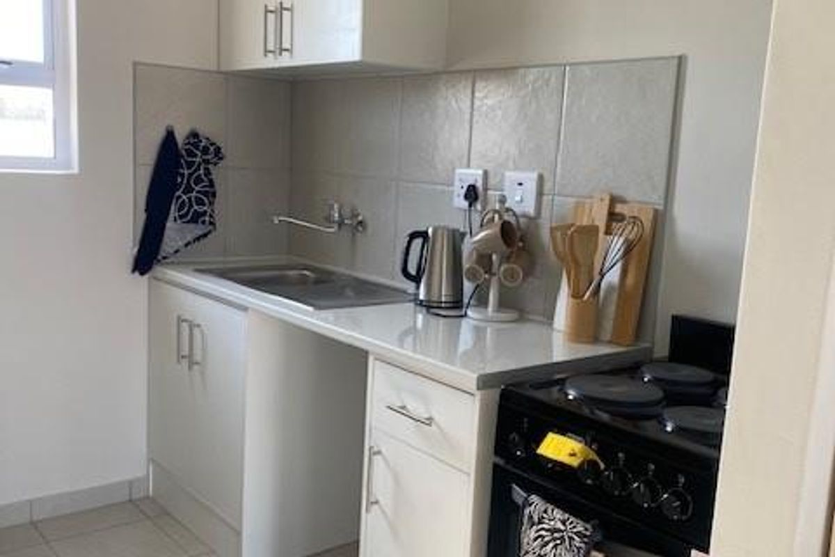 Compact kitchen featuring white cabinetry, tiled splashback, stainless steel sink, and a freestanding stove with ceramic floor tiles.