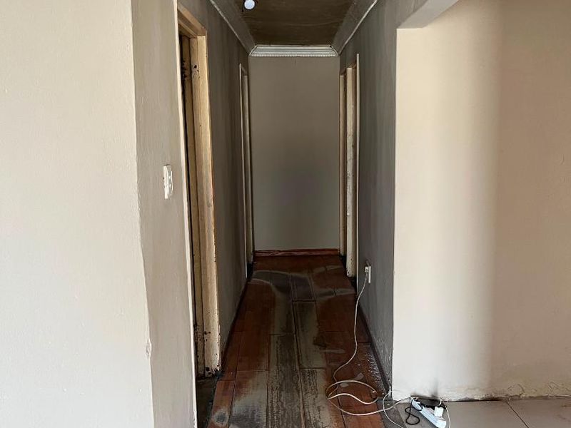 A vacant hallway featuring a mix of laminate and tiled flooring, with visible wear and ceiling finish requiring maintenance and repair.