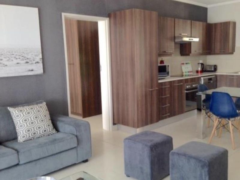 Open-plan living area featuring a modern kitchen with wood-finish cabinetry, integrated appliances, and tiled flooring, seamlessly connected to the lounge space.