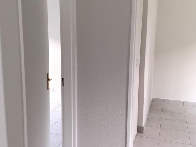 A clean, neutral hallway featuring light-colored floor tiles and white door frames, providing access to adjacent rooms in the apartment.