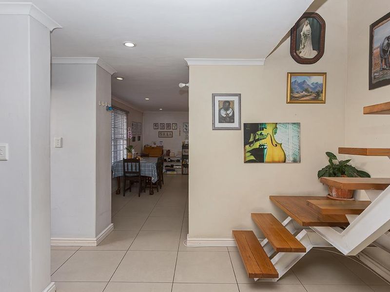 Open plan living area featuring modern tiled flooring and a distinctive floating staircase with timber treads, leading into a dining space.