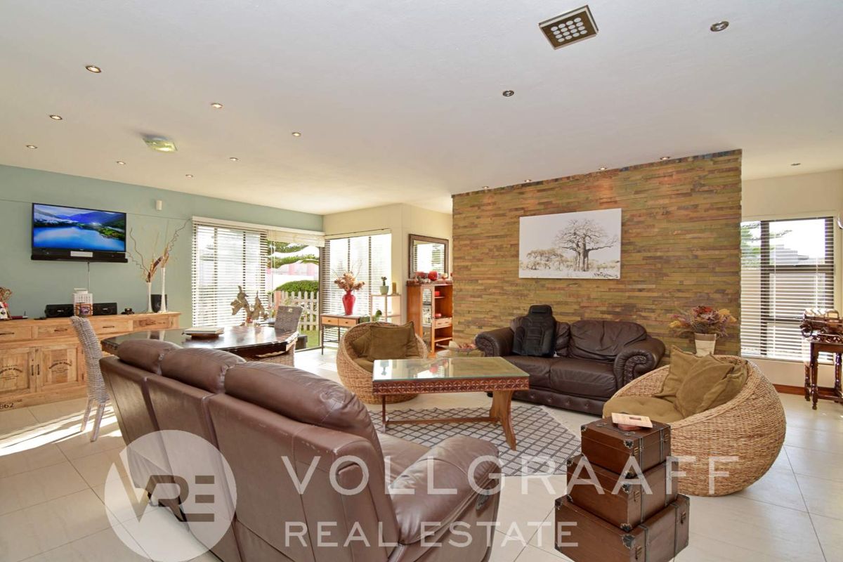 Spacious living room featuring a textured stone feature wall, tiled flooring, and recessed downlighting, offering a comfortable and well-lit area for relaxation.