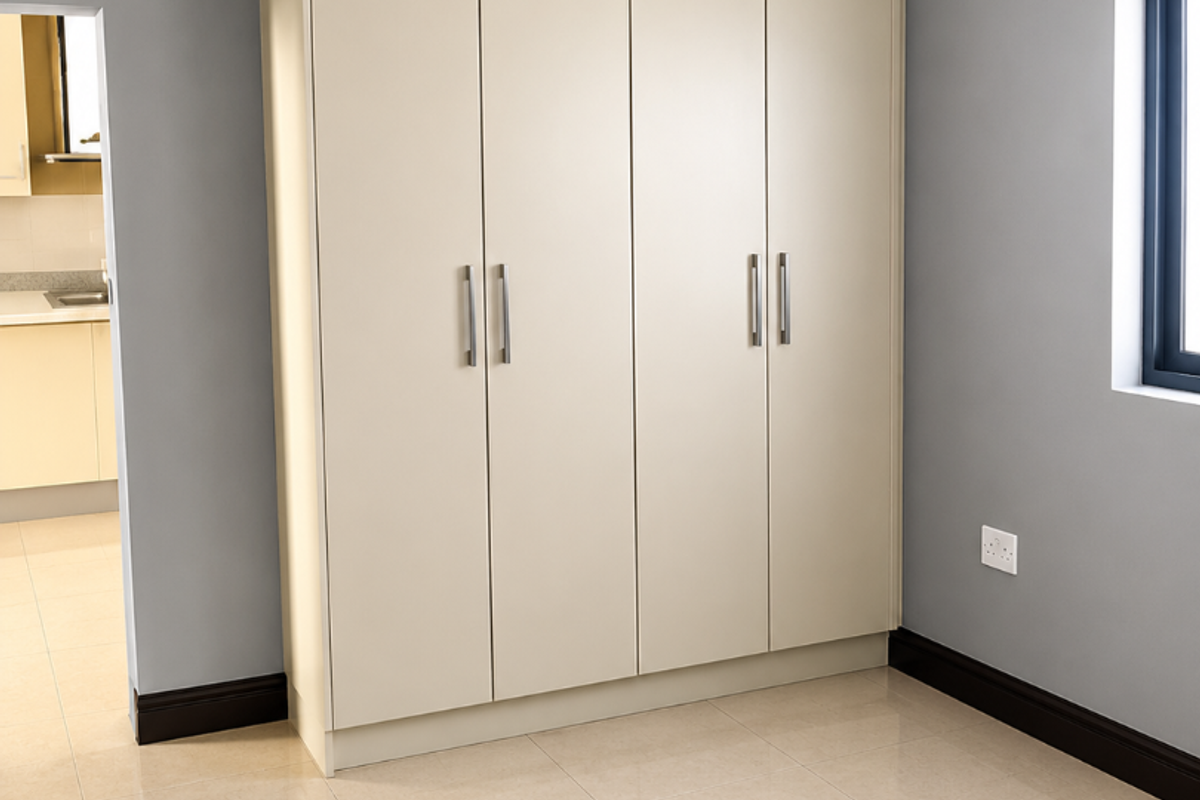 A clean, empty bedroom featuring neutral tiled flooring, grey walls, and a large, modern built-in wardrobe with sleek handles.