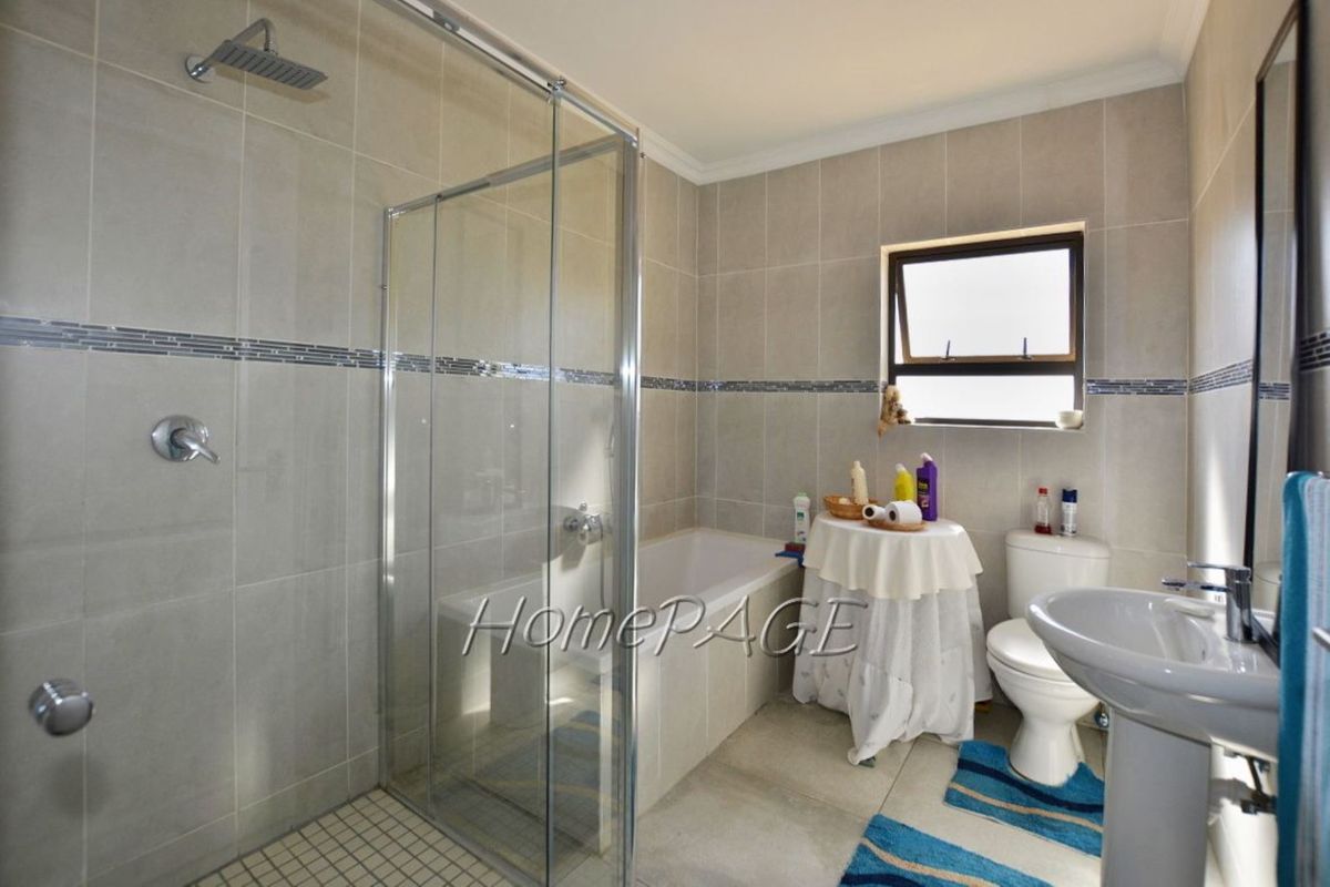 A modern bathroom featuring a glass-enclosed walk-in shower, a built-in bathtub, a pedestal sink, and a toilet with neutral wall tiling.