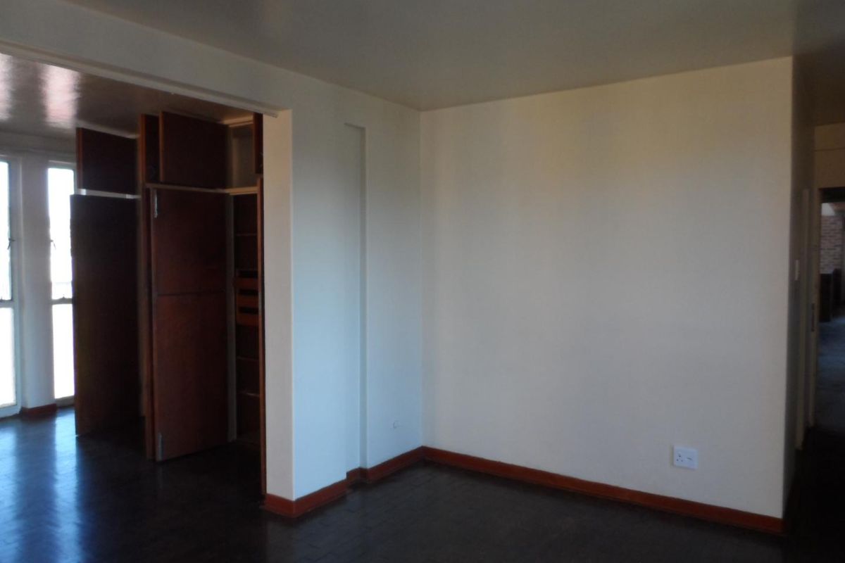 An empty bedroom featuring dark parquet flooring, built-in wooden cupboards, and neutral wall finishes.