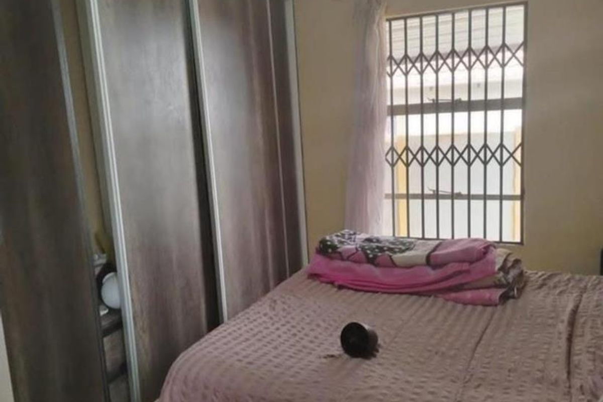 A bedroom featuring built-in sliding door cupboards and a window fitted with security bars.