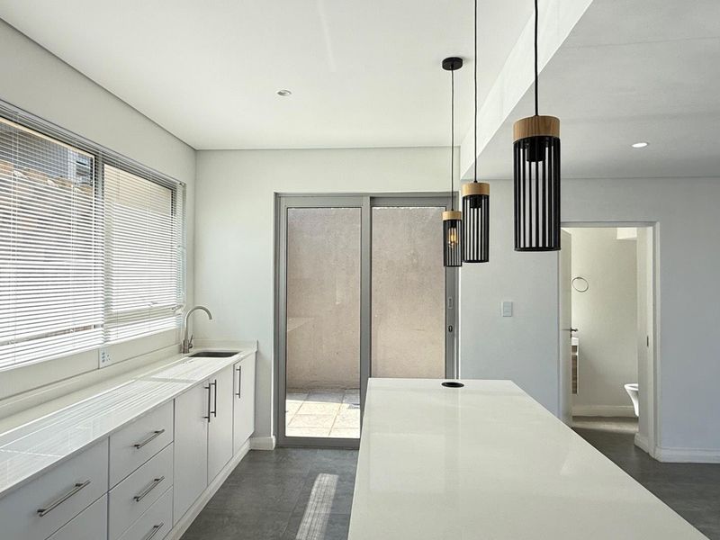Modern kitchen featuring a central island, sleek white cabinetry, quartz countertops, and direct access to an outdoor patio area.