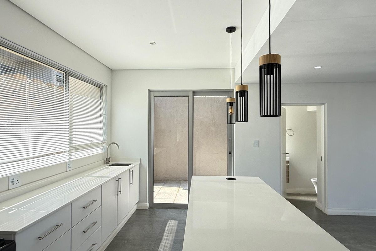 Modern kitchen featuring a central island, sleek white cabinetry, quartz countertops, and direct access to an outdoor patio area.