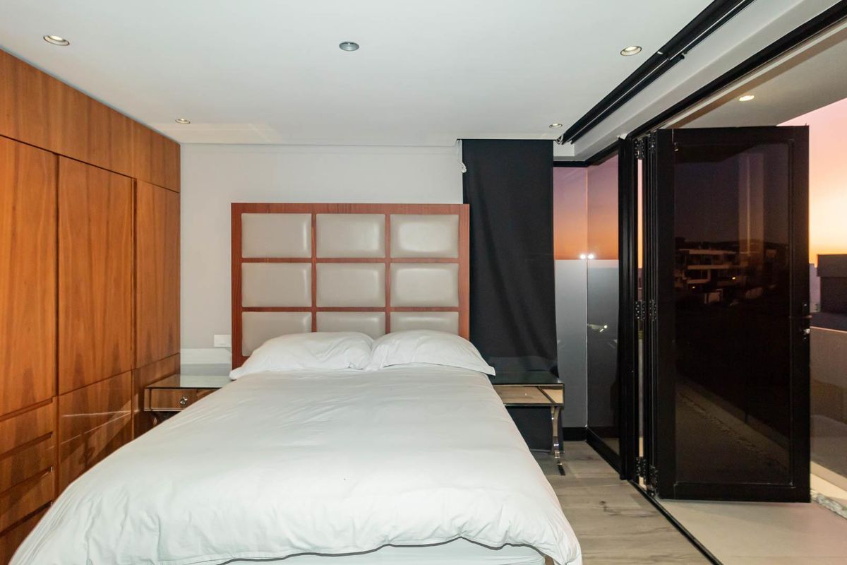 Modern bedroom featuring extensive built-in wooden cabinetry, recessed ceiling lighting, and large folding glass doors opening to an outdoor balcony area.