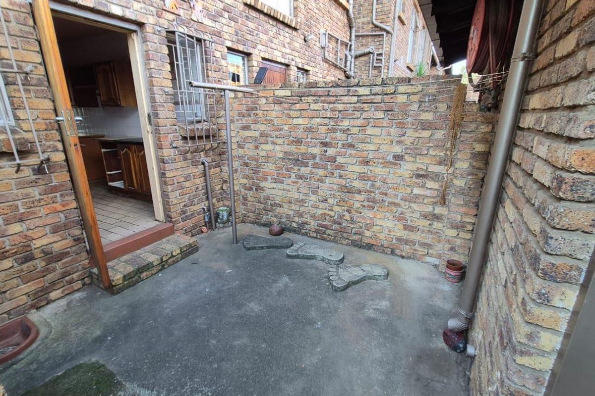 A small, private rear courtyard area featuring exposed brick walls, concrete flooring, and direct access to the kitchen interior.