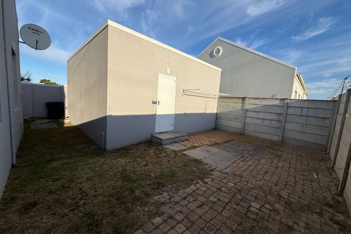 Rear exterior view of the property featuring a paved patio area, wall-mounted clothesline, and perimeter precast concrete walling.