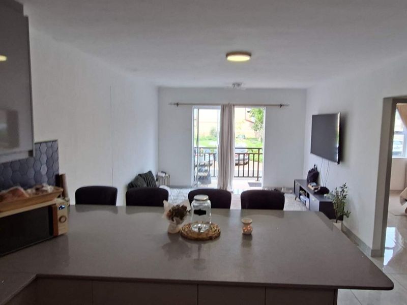 Open-plan living area featuring a modern kitchen with a central island, tiled floors, and direct access to a balcony through sliding glass doors.