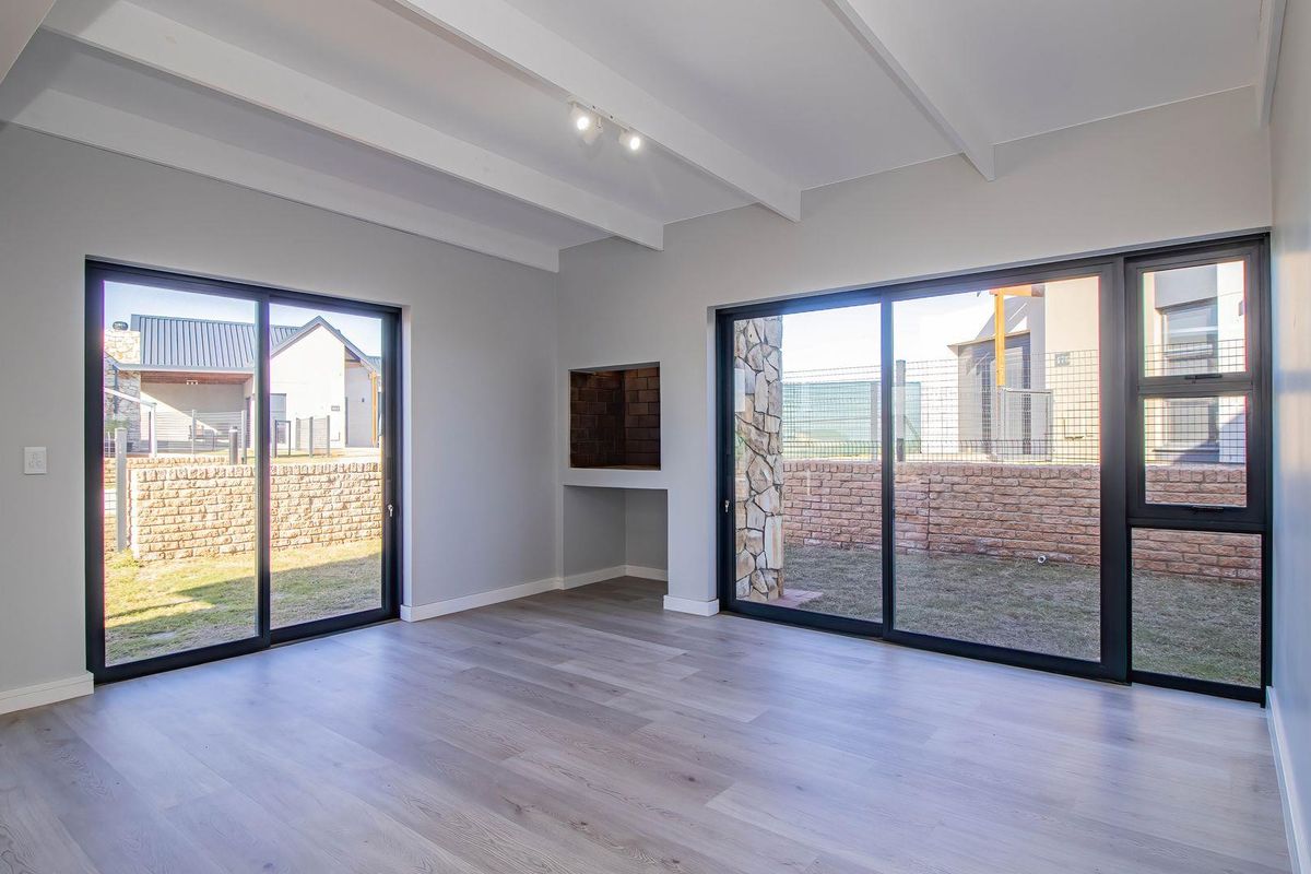 Bright and modern living area featuring exposed ceiling beams, wood-look flooring, and large sliding glass doors opening to a private garden.