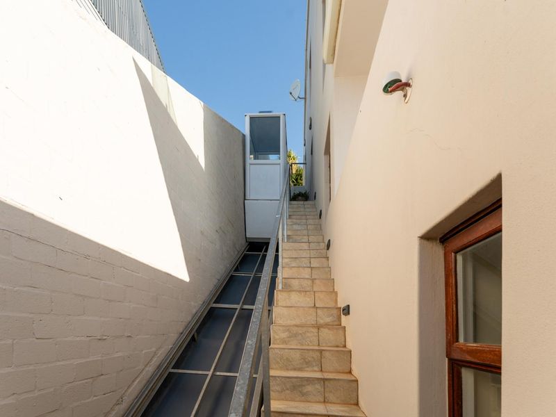 A narrow exterior side passage featuring a tiled staircase and a functional outdoor lift providing access between levels.