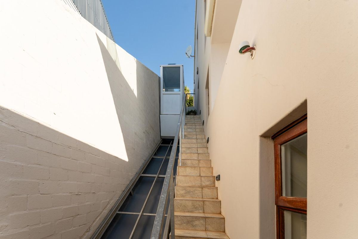 A narrow exterior side passage featuring a tiled staircase and a functional outdoor lift providing access between levels.