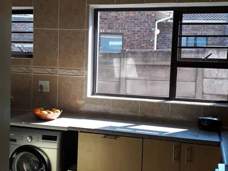 A functional kitchen area featuring tiled splashbacks, laminate cabinetry, stone-look countertops, and tiled flooring with space for a washing machine.