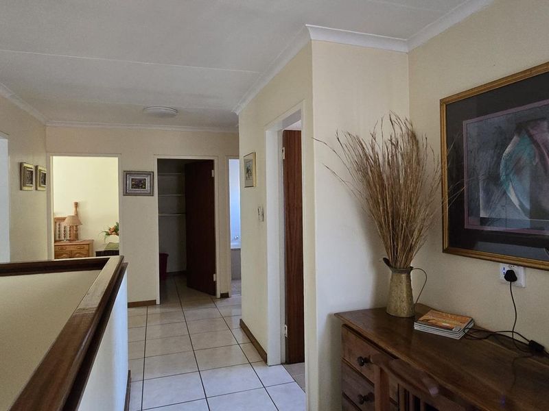 A well-lit hallway featuring tiled flooring and a wooden balustrade, providing access to multiple rooms within the home.