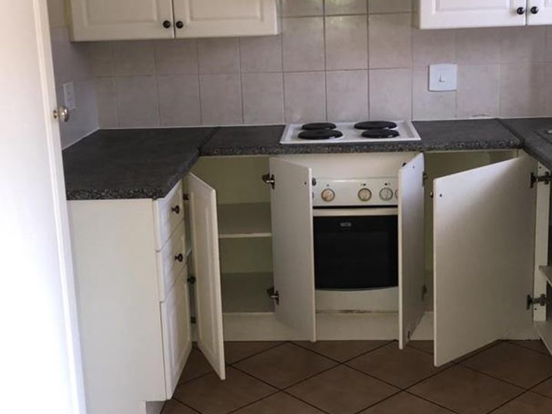 A dated kitchen featuring white cabinetry, dark laminate countertops, an electric hob, and tiled flooring, currently showing signs of wear and maintenance needs.