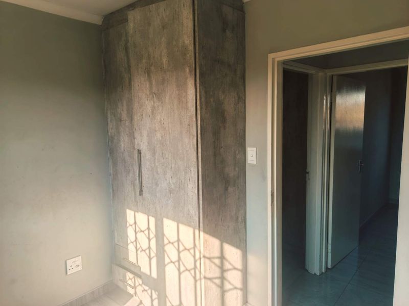 A bedroom featuring a built-in wardrobe with a textured finish, tiled flooring, and a security gate, presenting a clean and functional space.