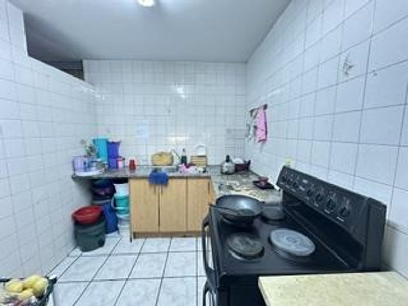 A functional kitchen featuring tiled walls and flooring, laminate countertops, a stainless steel sink, and a freestanding electric stove.