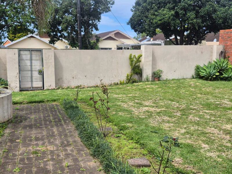A private rear garden featuring a paved walkway, a raised concrete planter, and a combination of plastered and face-brick perimeter boundary walls.