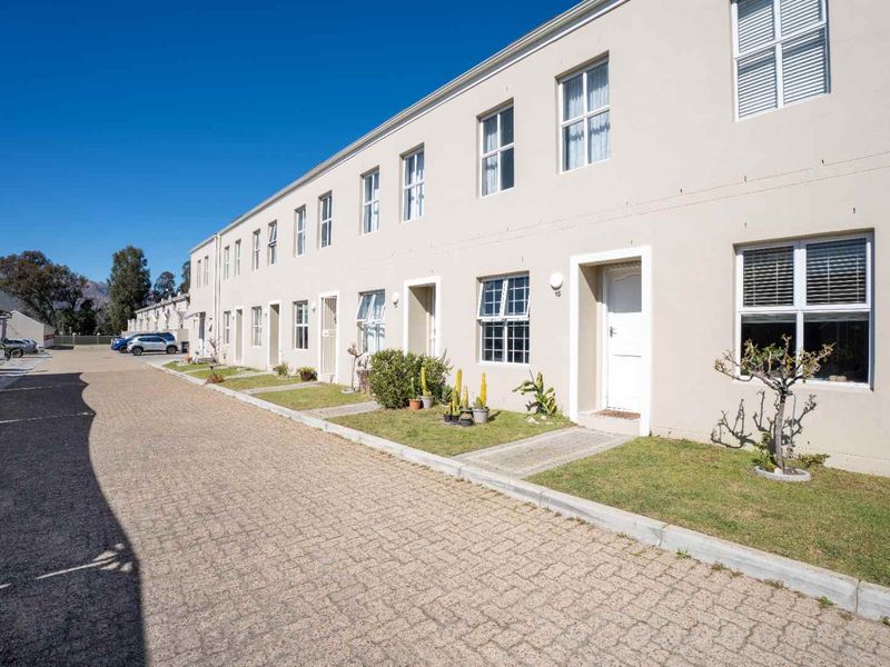 Exterior view of a multi-unit apartment complex featuring paved driveway access, small grass verges, and uniform building facade with multi-pane windows.