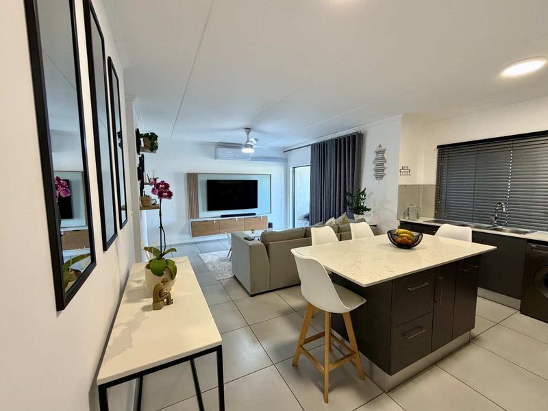 Modern open-plan living area featuring a sleek kitchen with a stone-topped island, tiled flooring, and integrated air conditioning, creating a bright and functional space.