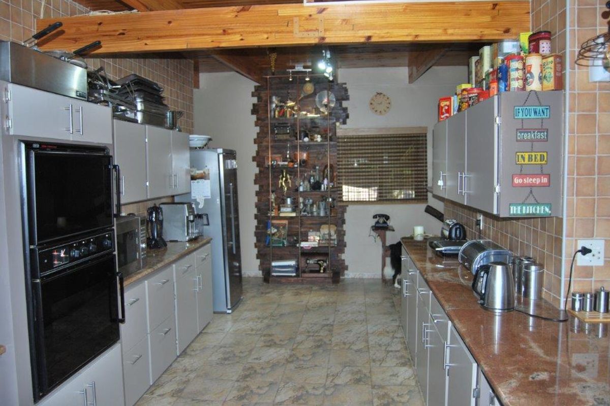 A functional kitchen featuring built-in cabinetry, integrated oven, and tiled surfaces, with exposed timber ceiling beams and a decorative brick feature wall.