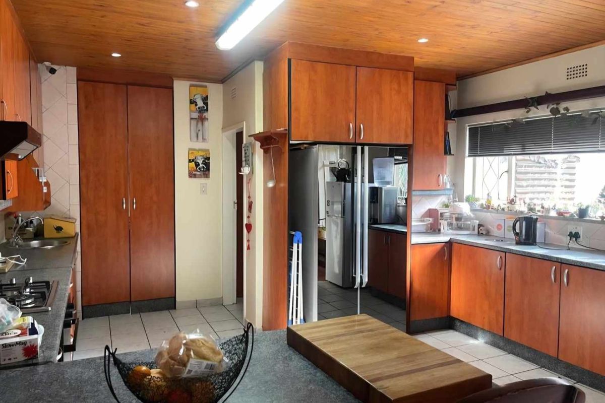 A functional kitchen featuring wood-finish cabinetry, laminate countertops, a built-in hob, and a timber-paneled ceiling with integrated lighting.