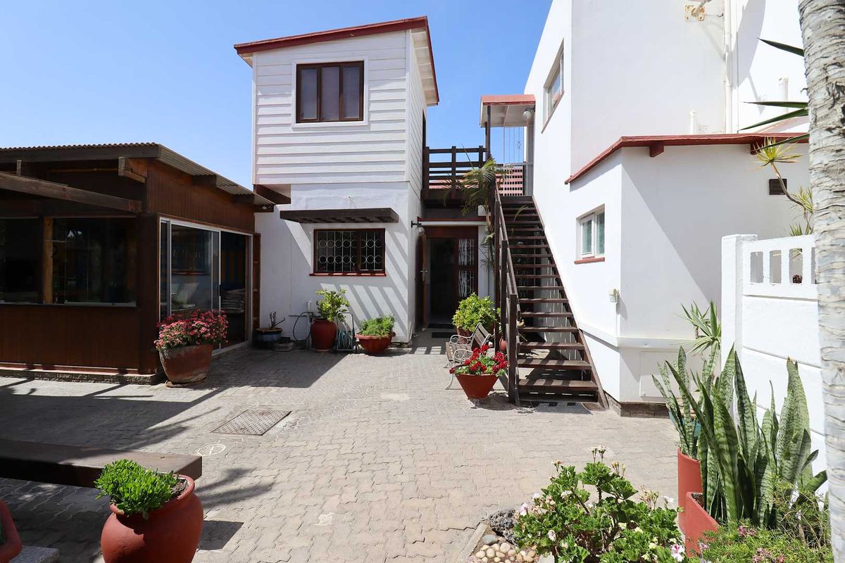 A paved rear courtyard featuring an external timber staircase leading to an upper balcony, with white rendered walls and timber-clad architectural details.