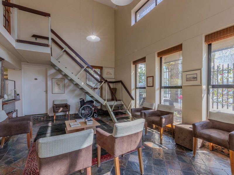 Spacious living area featuring double-height ceilings, slate tile flooring, and a prominent staircase leading to a mezzanine level with abundant natural light.