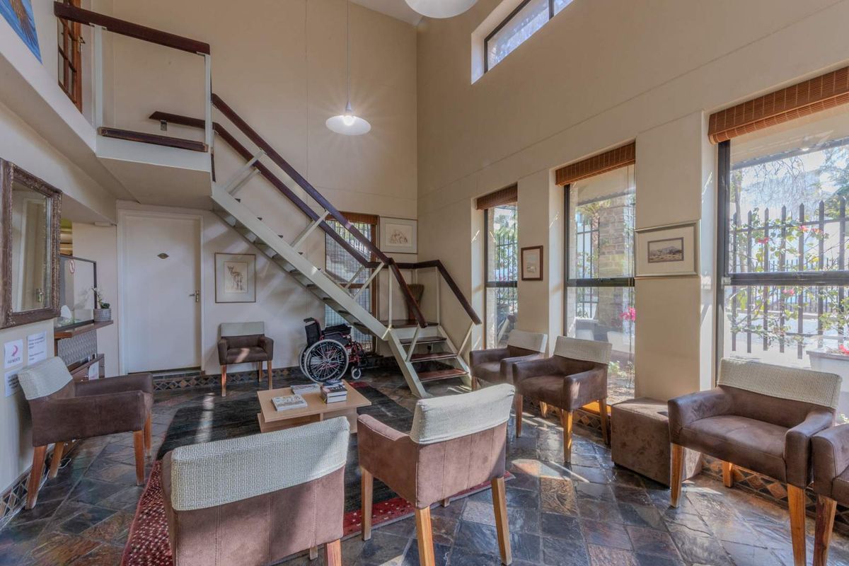 Spacious living area featuring double-height ceilings, slate tile flooring, and a prominent staircase leading to a mezzanine level with abundant natural light.
