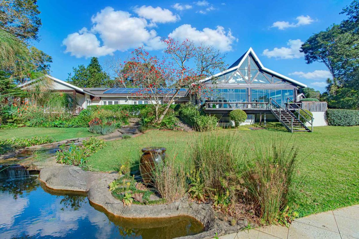 Rear view of a spacious house featuring a large timber deck, expansive glass windows, solar panels, and a beautifully landscaped garden with a pond.