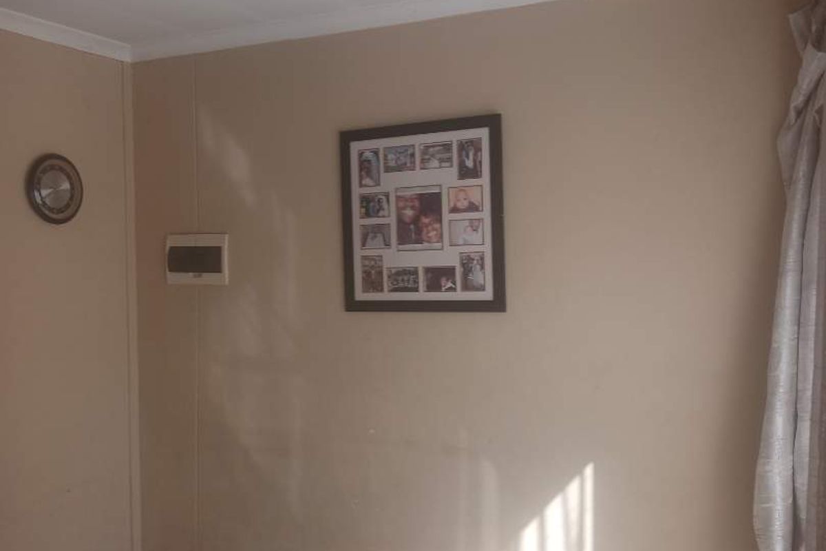 A simple bedroom interior featuring tiled flooring and neutral wall finishes with natural light entering from the side window.