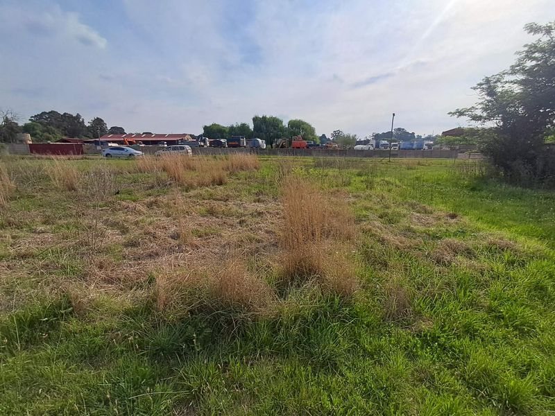 An expansive open plot of land on a small holding, featuring natural grass cover and a perimeter boundary wall.