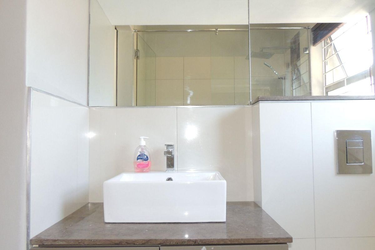 Modern bathroom featuring a white vessel sink on a stone vanity, large wall mirror, and a glass-enclosed shower with concealed cistern flush plate.