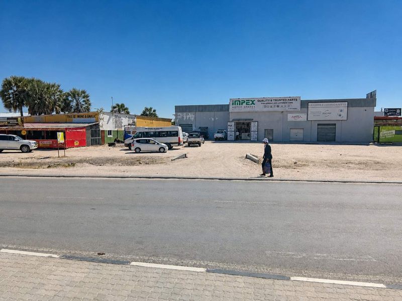 Street-level view of a commercial property featuring multiple business units, roller shutter doors, and an unpaved parking area.